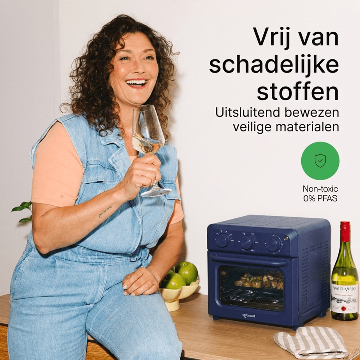 Smiling woman with wine glass beside a blue oven and text about non-toxic materials.
