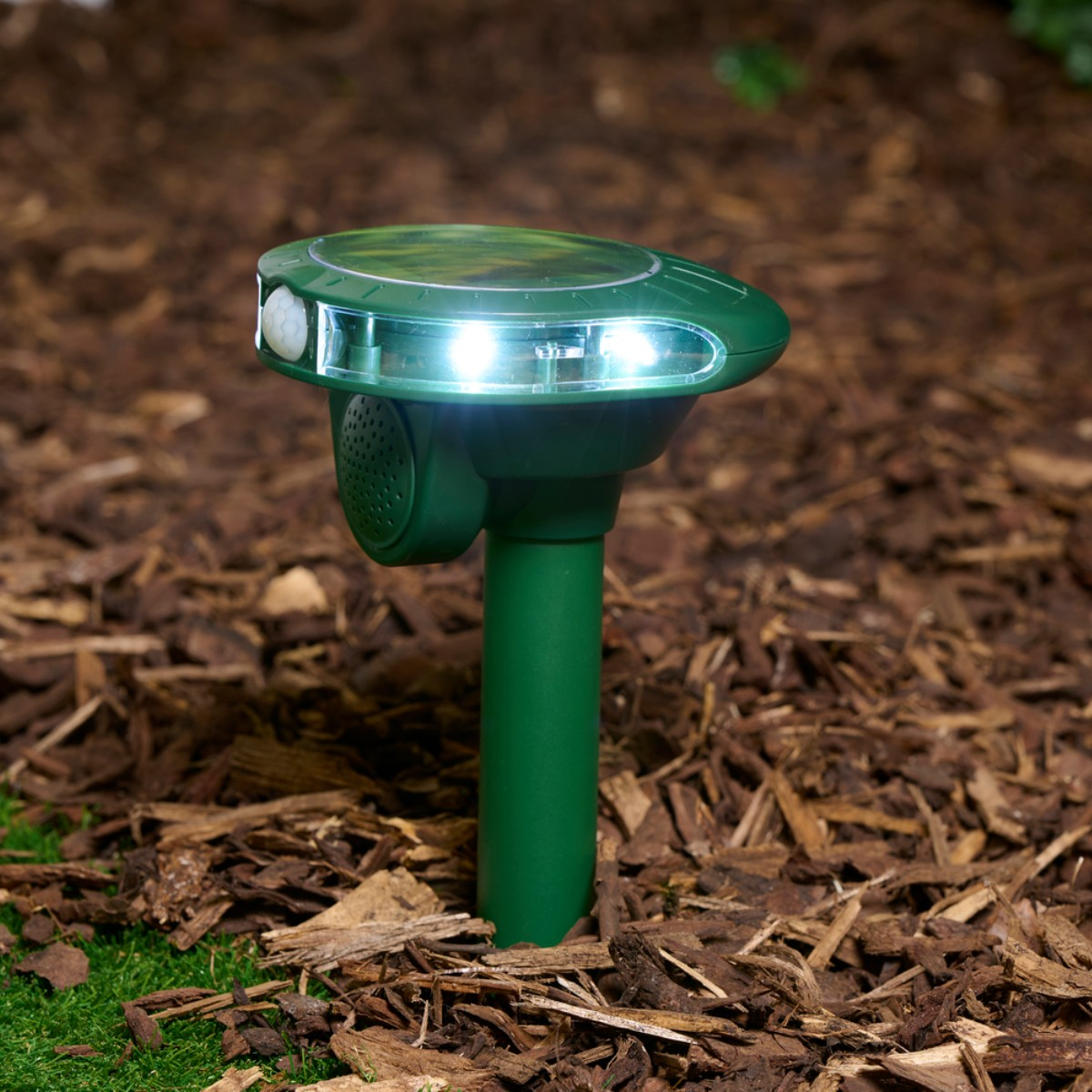 Groene solarlamp met bewegingssensor en luidspreker in boomschors.