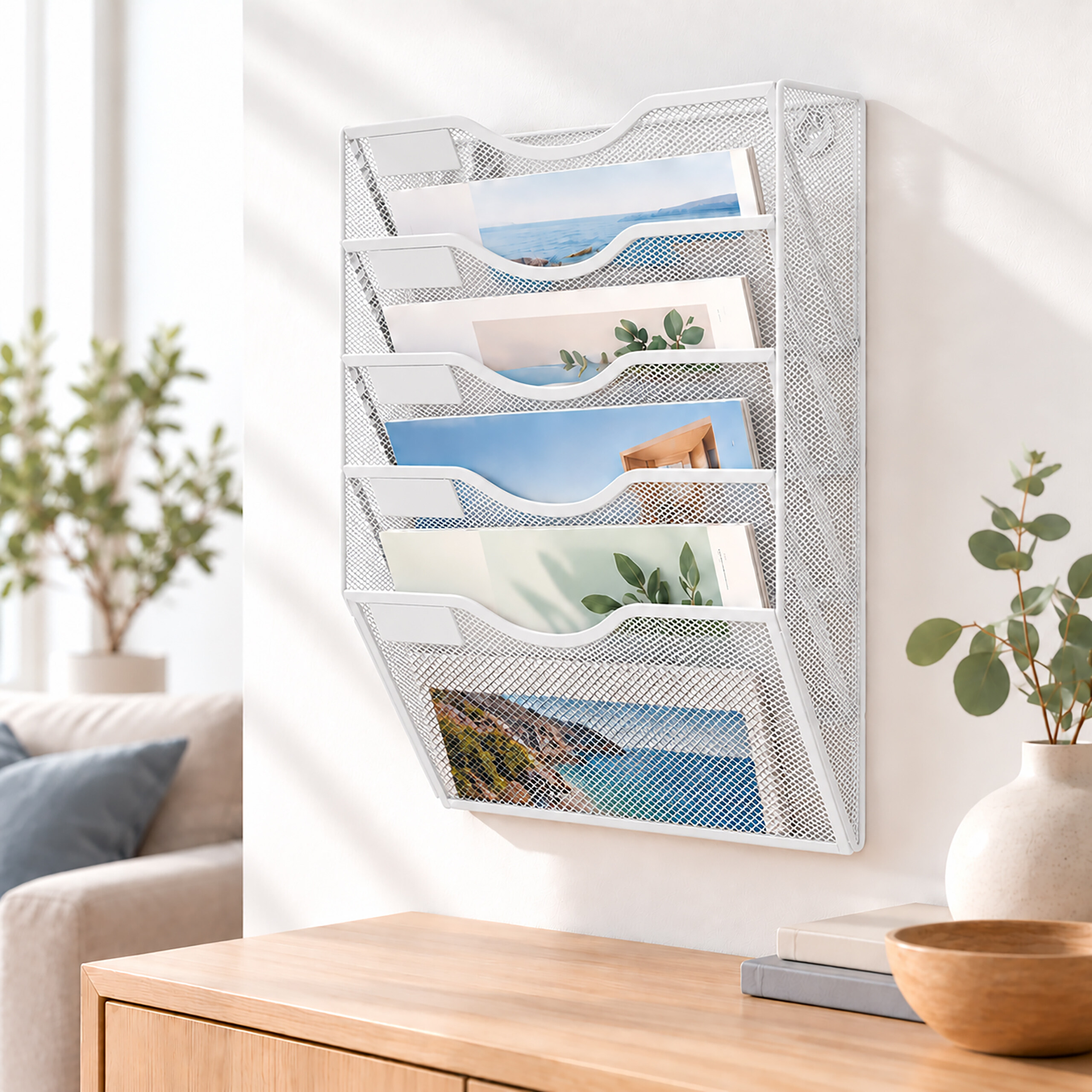 Ein weißer Netz-Wand-Aktenorganizer hält fünf Mappen mit Naturbildern über einer Holzkonsole.