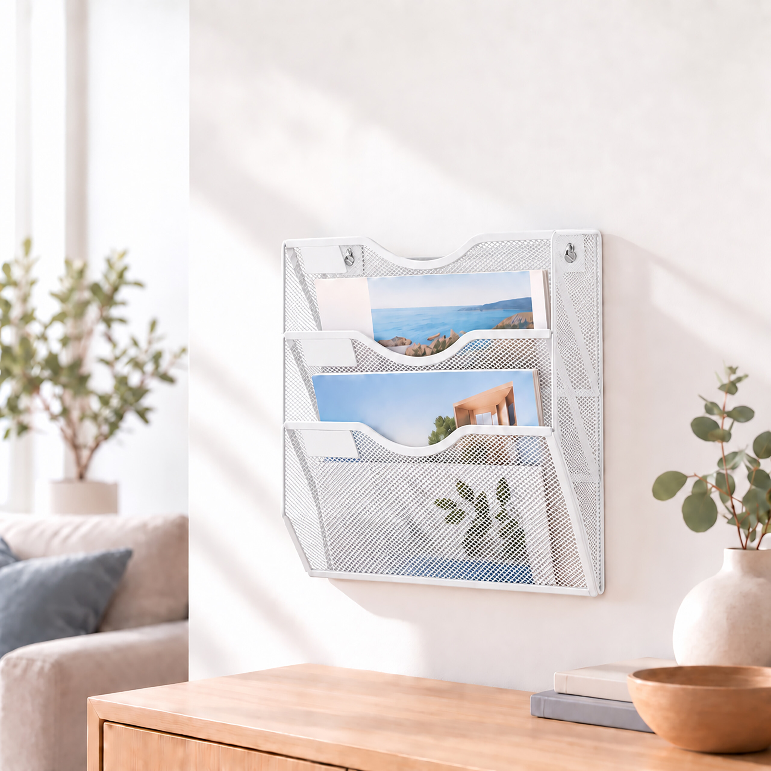 Ein weißer Wand-Briefsammler aus Metall hängt an einer Wand mit Zeitschriften, Schreibtisch und Pflanze.