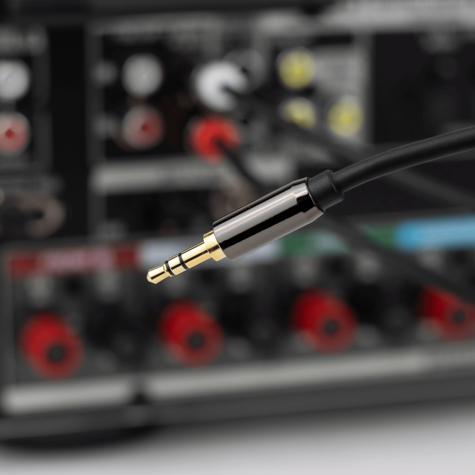 Primer plano de un conector de audio de 3.5 mm con un receptor de audio borroso al fondo.