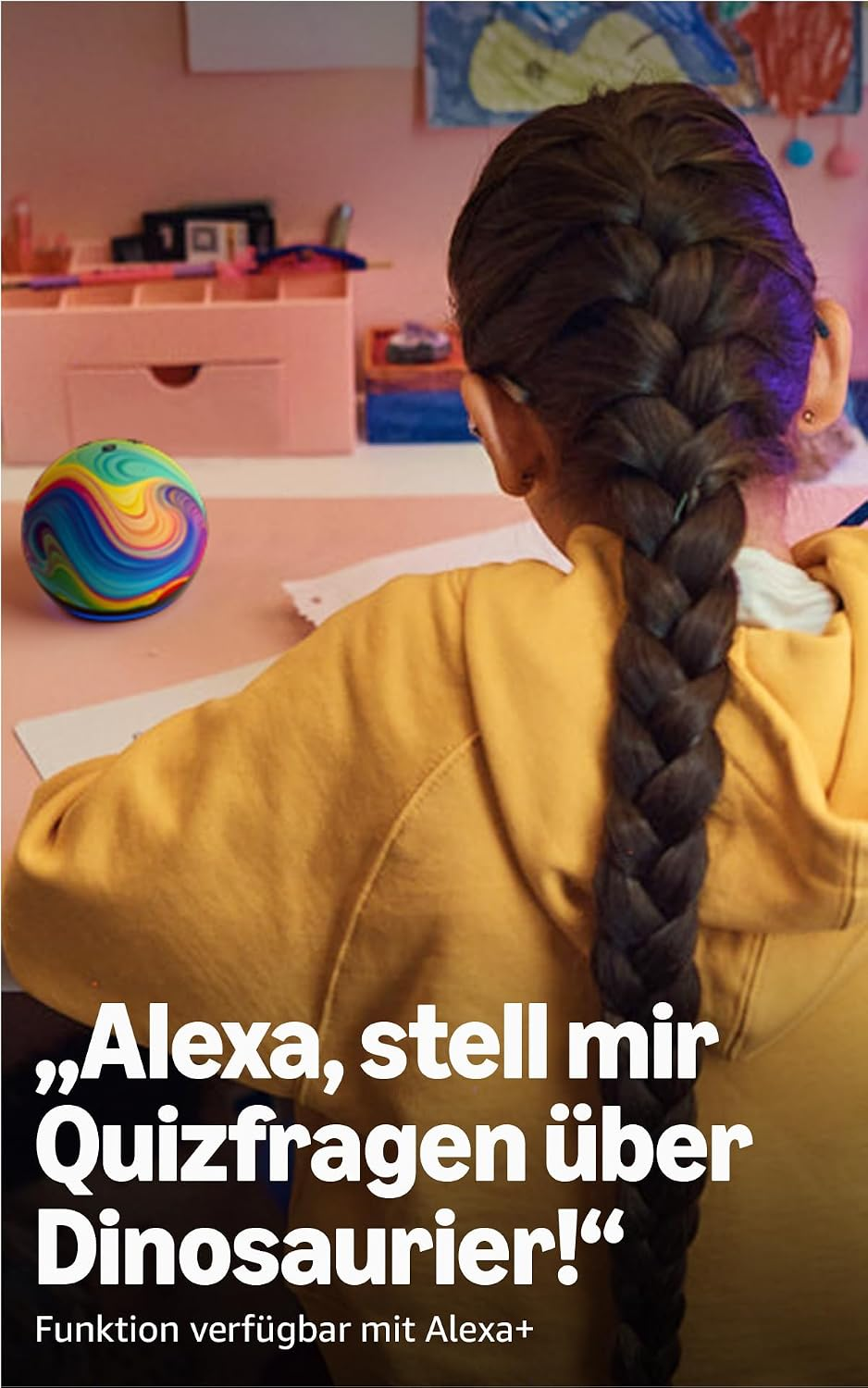 Mädchen mit langem geflochtenen Zopf sitzt an rosa Schreibtisch mit buntem Ball und schreibt.