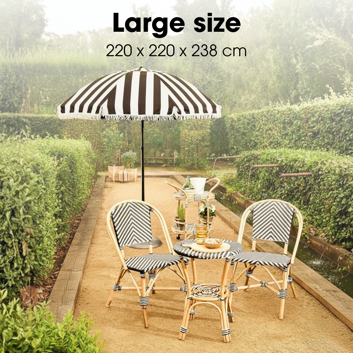 Garden set with black-and-white striped umbrella, two chairs, and a table in greenery.