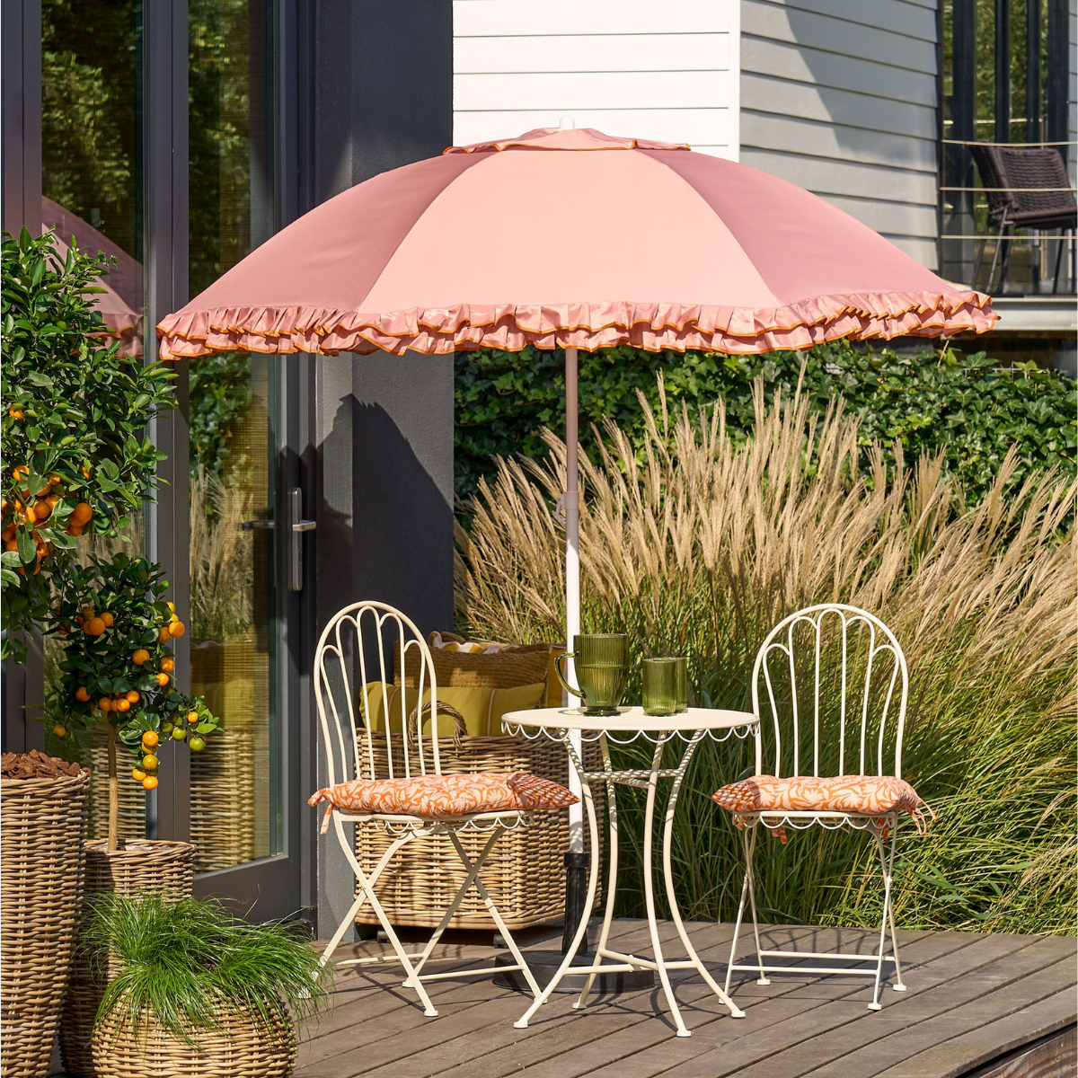 Pink parasol, table and two chairs with cushions on a wooden patio.