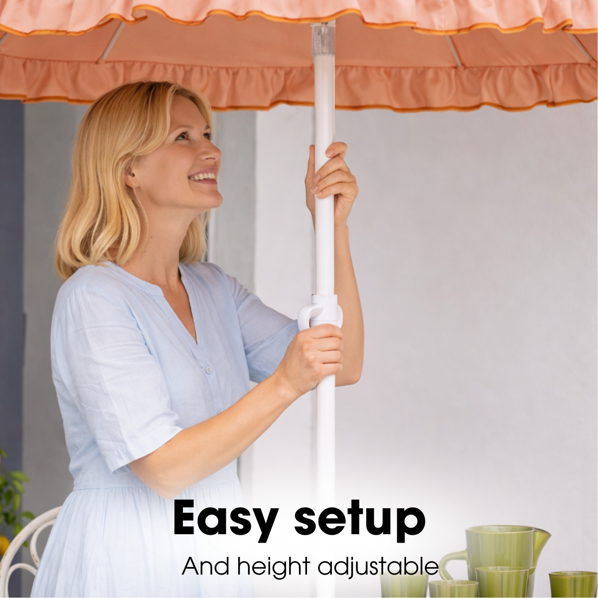 A blonde woman in a light blue dress adjusts a peach-colored parasol outdoors.