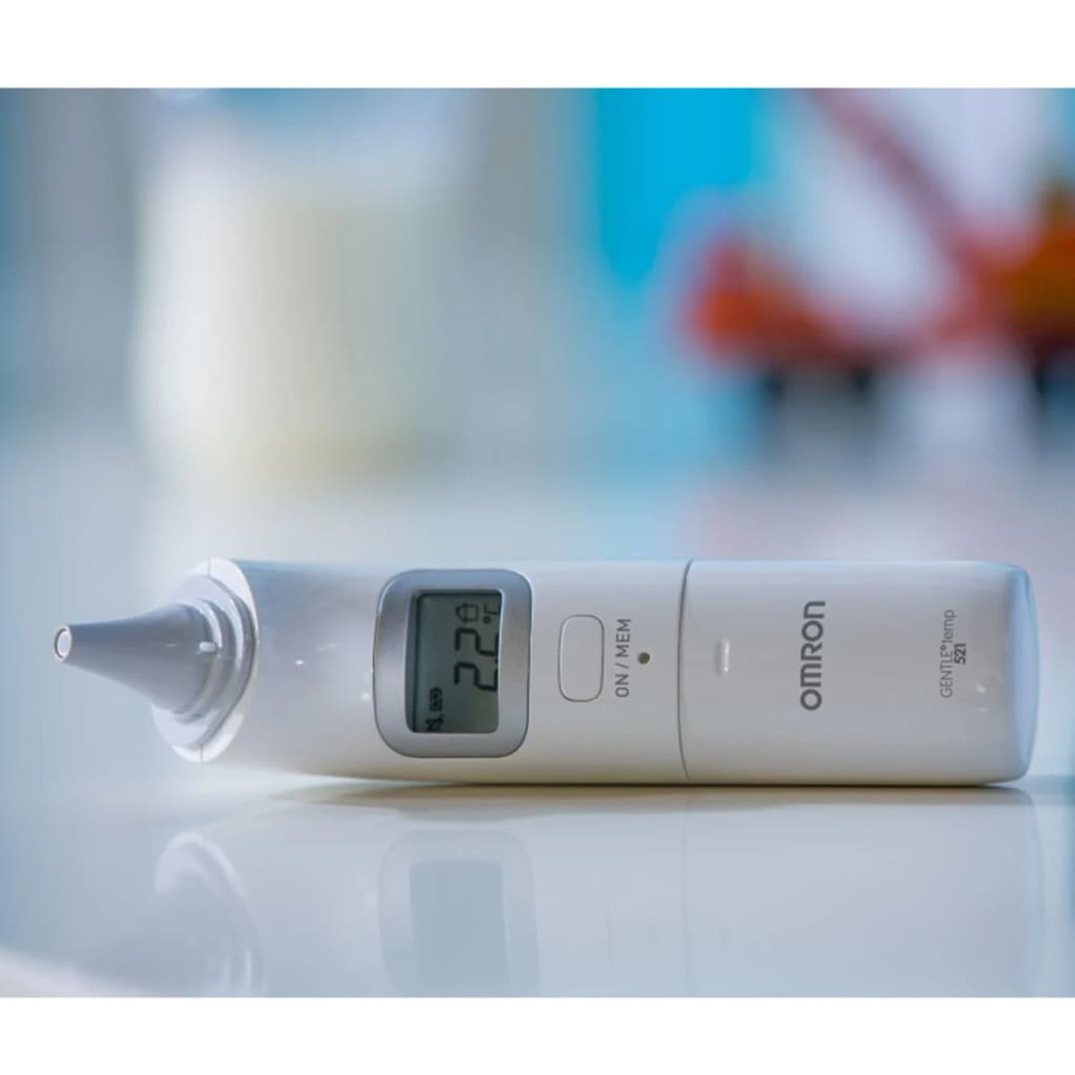 Ein weißes Omron-Ohrthermometer liegt horizontal auf einer weißen Oberfläche mit unscharfem Hintergrund.