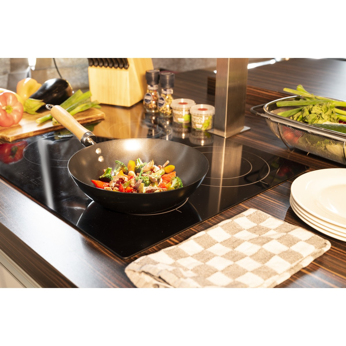 Wokpan met groenten op een glanzende inductiekookplaat in een moderne keuken.