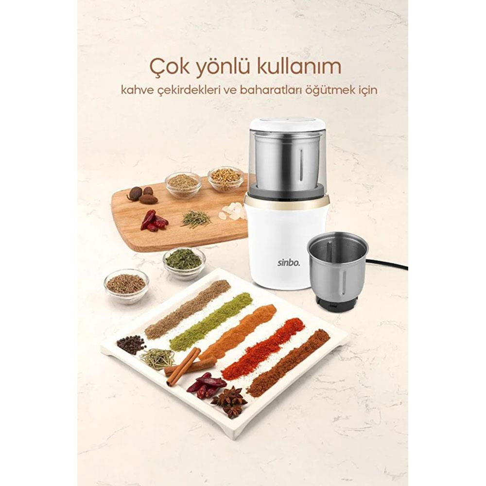 Beyaz tabak ve tahta üzerinde çeşitli baharatlar ve otlar bulunan beyaz kahve öğütücü.