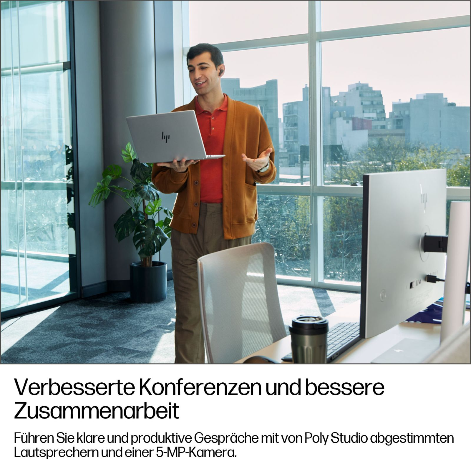 Un homme dans un bureau tient un ordinateur portable devant une grande fenêtre.