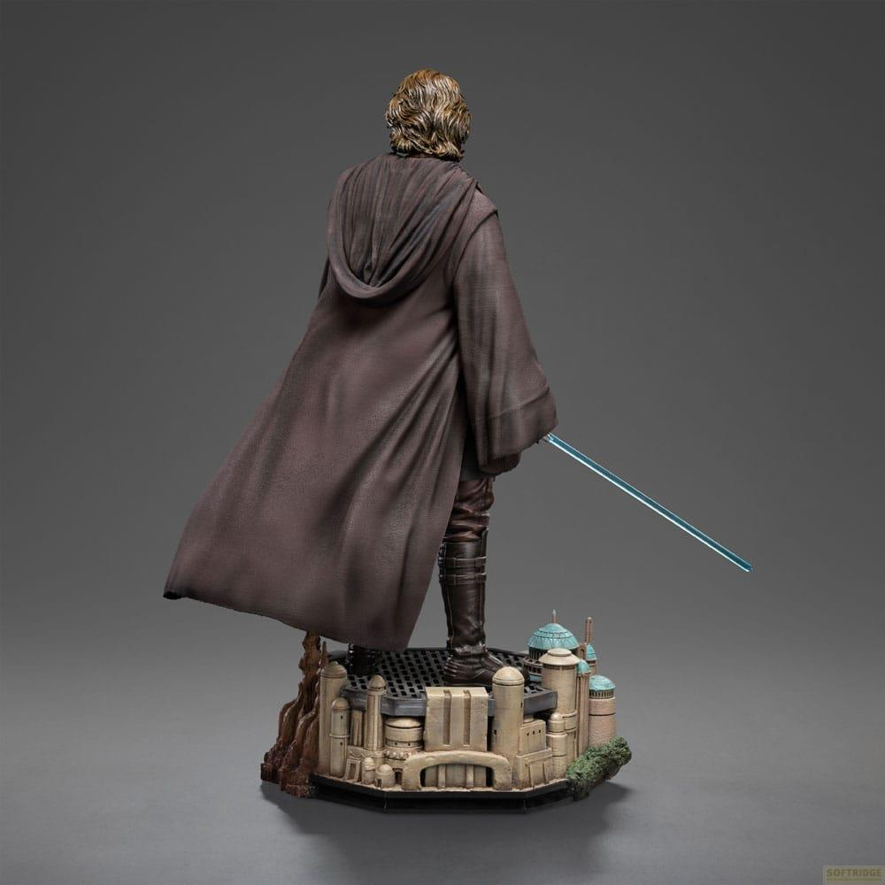 Vista posteriore di un'action figure con mantello e tunica marrone, con spada laser blu su una base urbana.