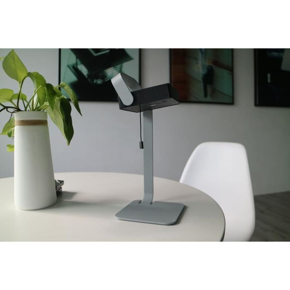 Eine graue moderne Lampe und eine Pflanze in einer weissen Vase stehen auf einem Tisch.