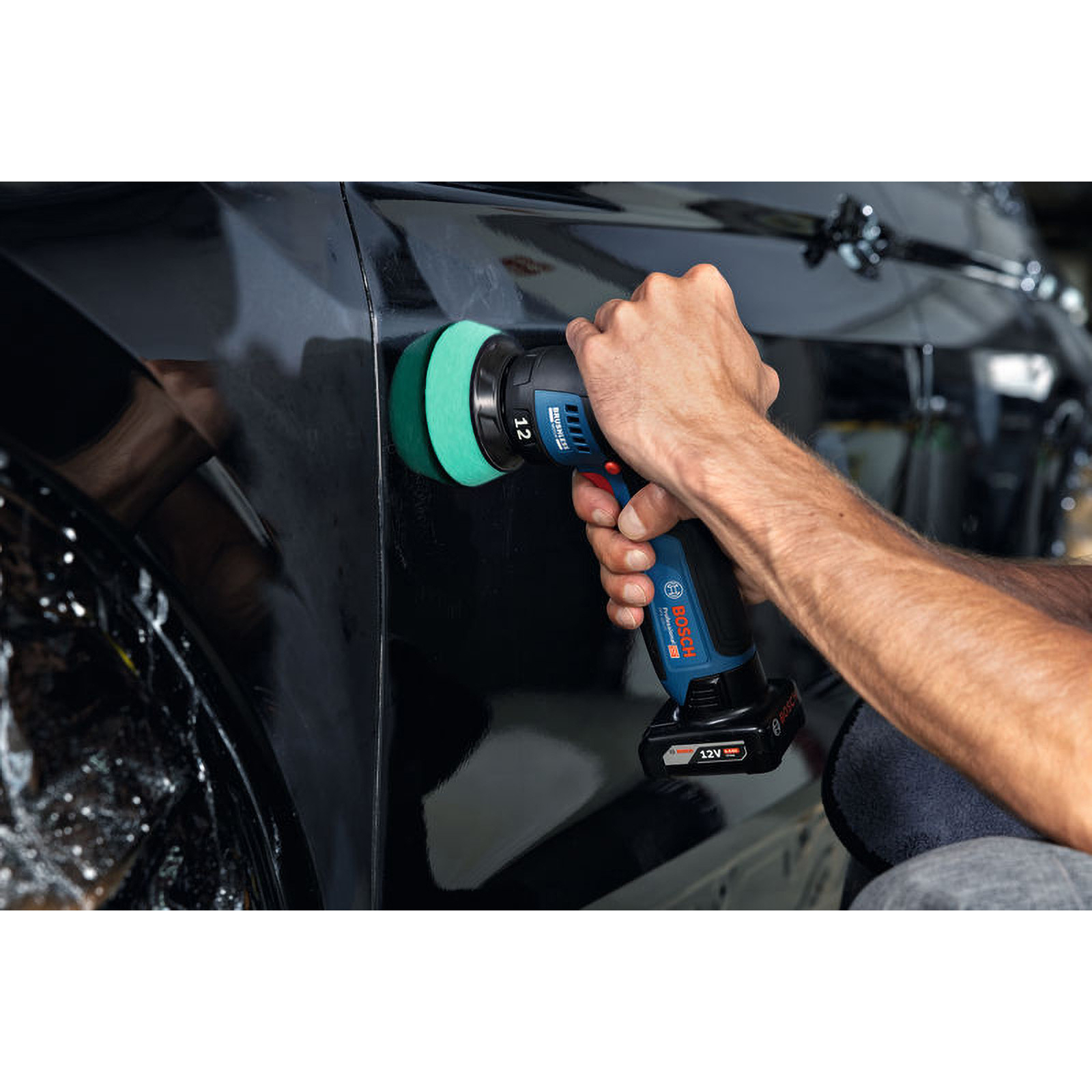 Person poliert die schwarze Karosserie eines Autos mit einer kleinen blauen Akku-Poliermaschine.