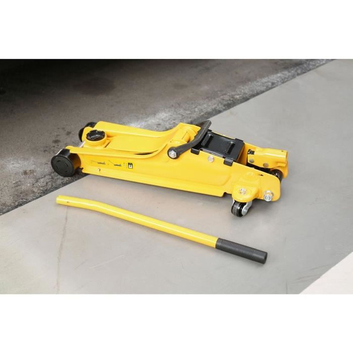 Ein gelber hydraulischer Wagenheber liegt mit seiner separaten gelben Stange auf einem grauen Betonboden.