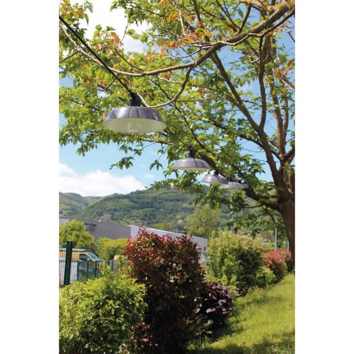 Lichterketten hängen unter einem Baum im Garten mit Blick auf grüne Hügel.