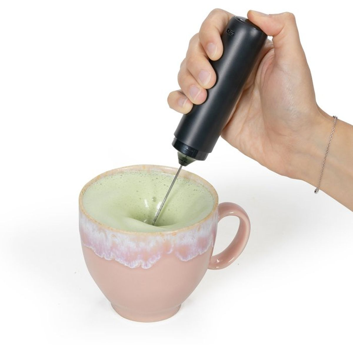 Una mano usa un montalatte nero per mescolare il matcha verde in una tazza rosa.