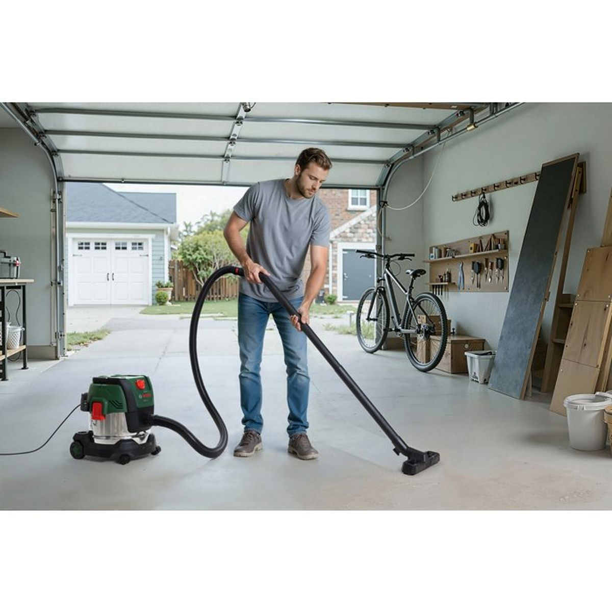 Ein Mann reinigt in einer Garage den Betonboden mit einem grüne-schwarzen Nass-/Trockensauger.