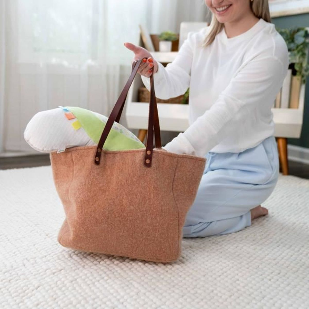 Eine kniende Frau packt eine grüne Babytasche auf einem hellen Teppich aus.
