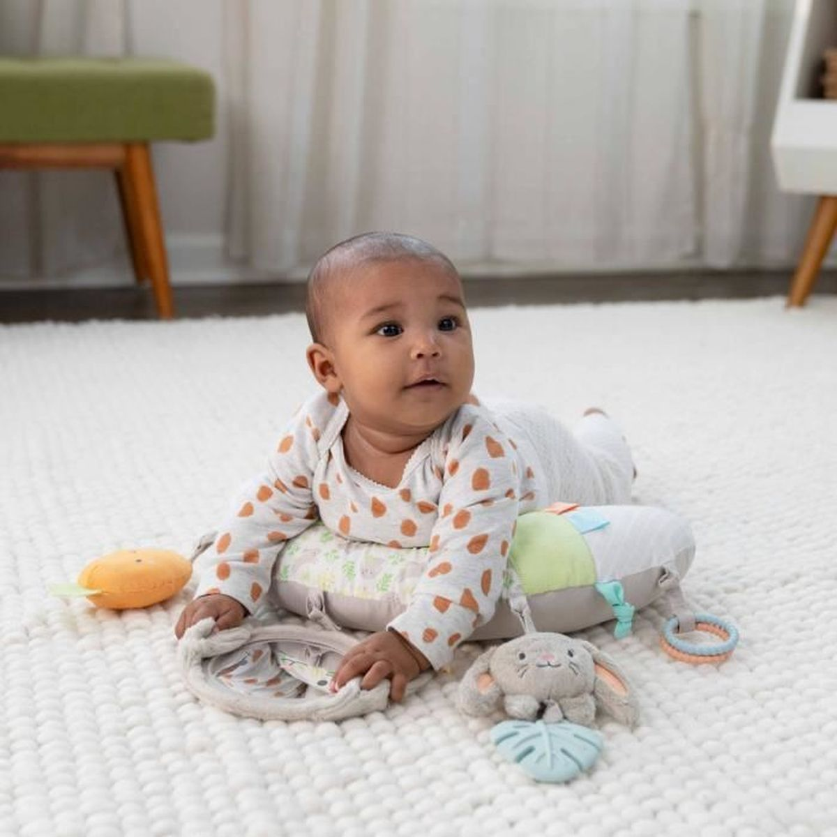 Ein Baby liegt auf einem Bauchlagunenkissen mit Spielzeug auf einem weißen Teppich.