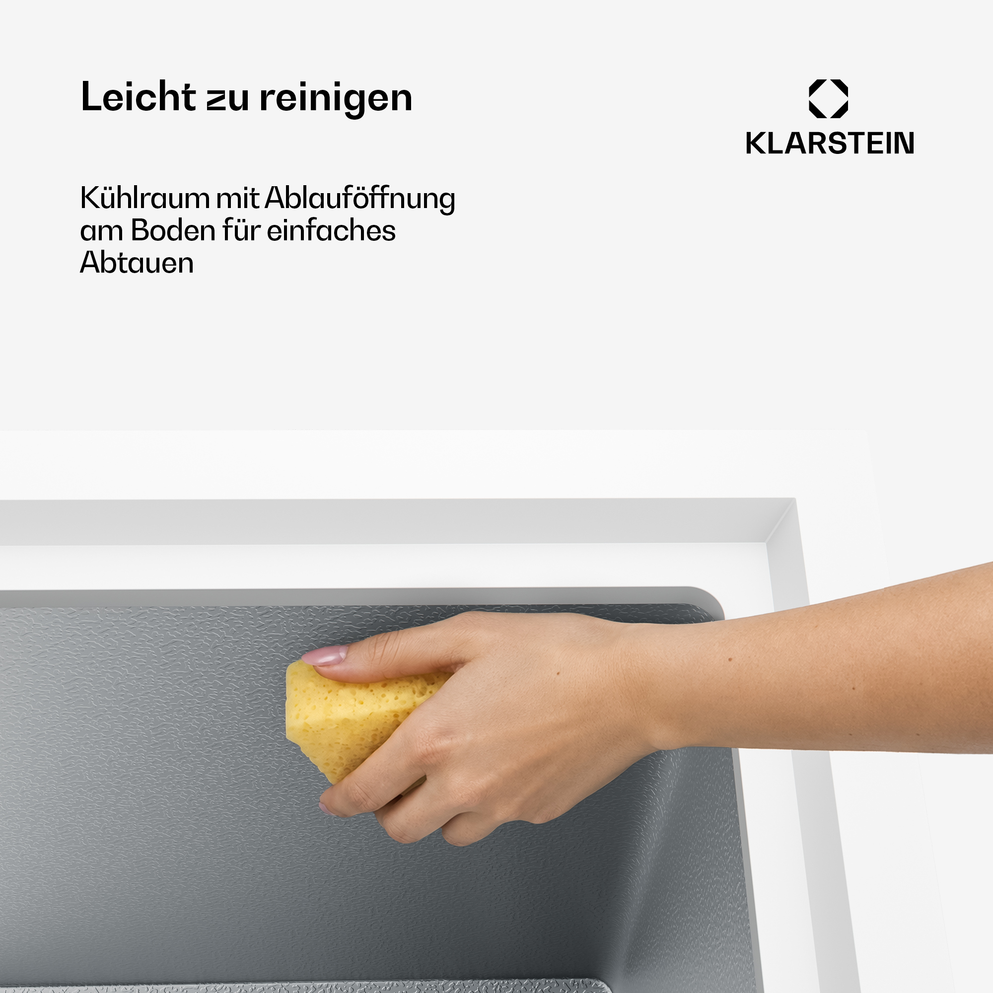 Eine Hand reinigt das graue Innere eines weißen Kühlgeräts mit einem gelben Schwang.