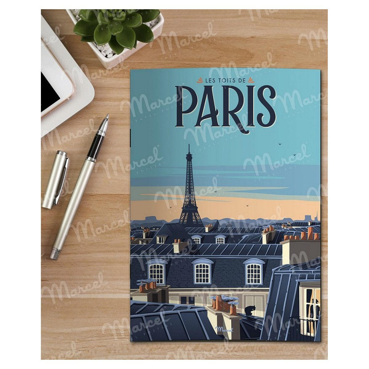 Ein Paris-Poster auf einem Holztisch mit Stift und Pflanze.