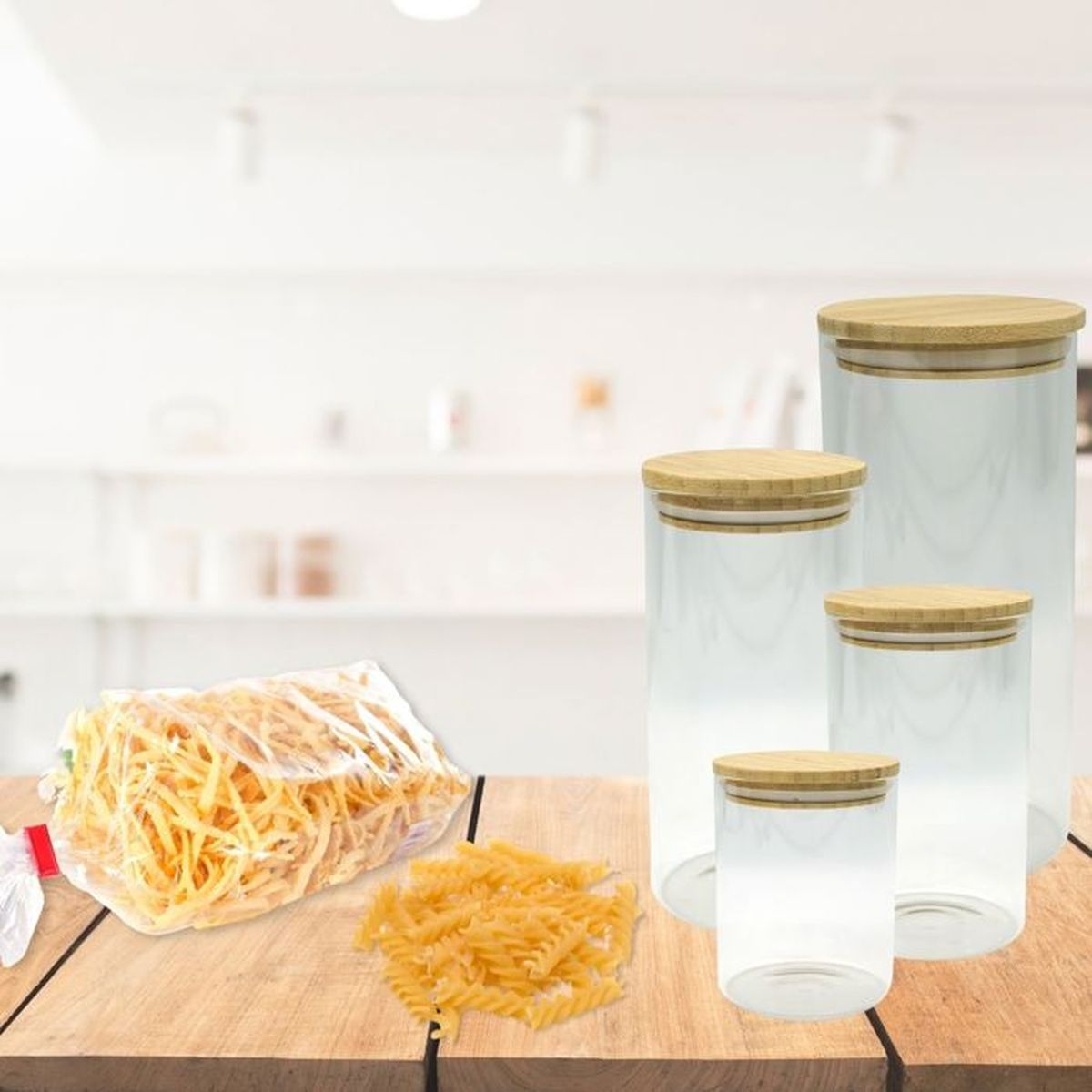 Vier Vorratsgläser aus Glas mit Bambusdeckel stehen auf einem Holztisch neben einer Tasche und Nudeln.