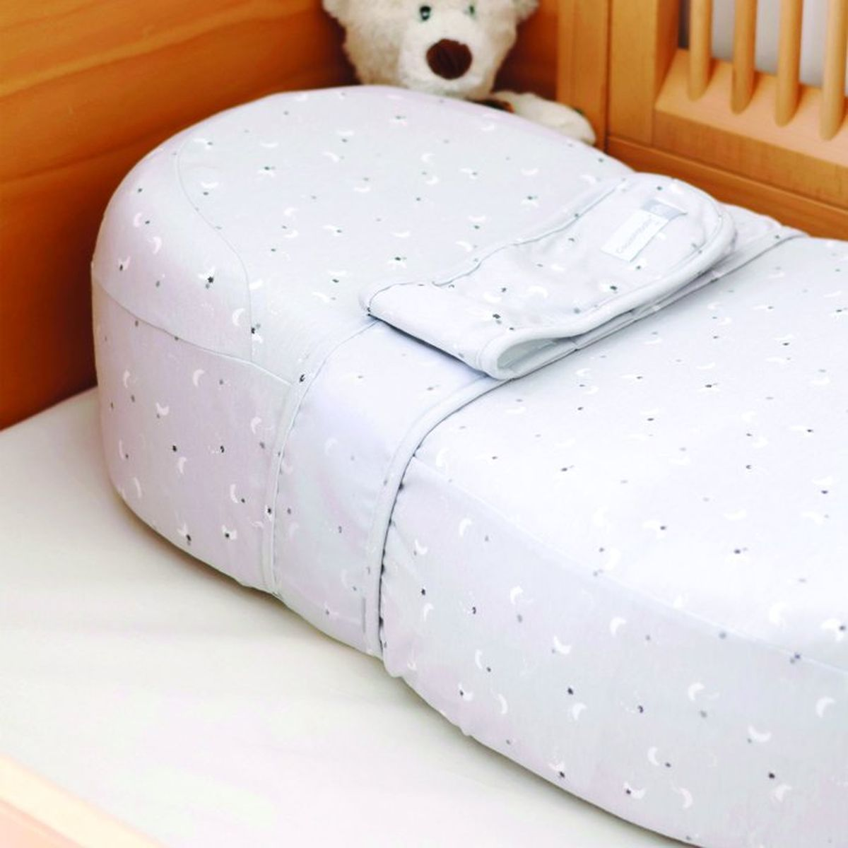Ein graues Babybettnestchen mit Sternenmuster im Holzbett.
