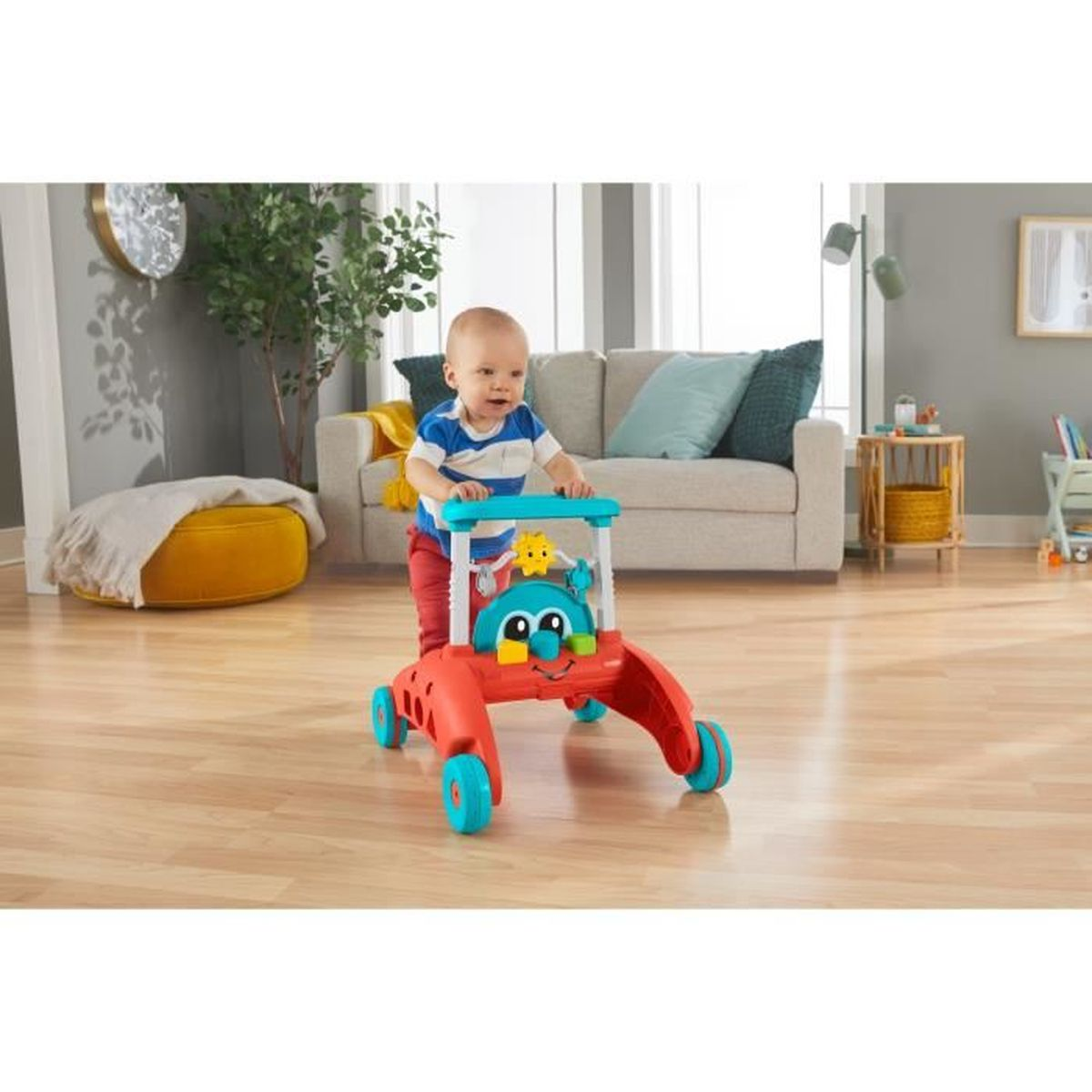 Ein Baby schiebt einen bunten Lauflernwagen auf einem Holzfussboden in einem hellen Wohnzimmer.