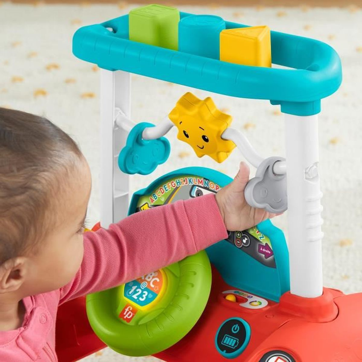 Kleinkind in rosa Oberteil spielt mit buntem Lernspielzeug mit Lenkrad und Formen.
