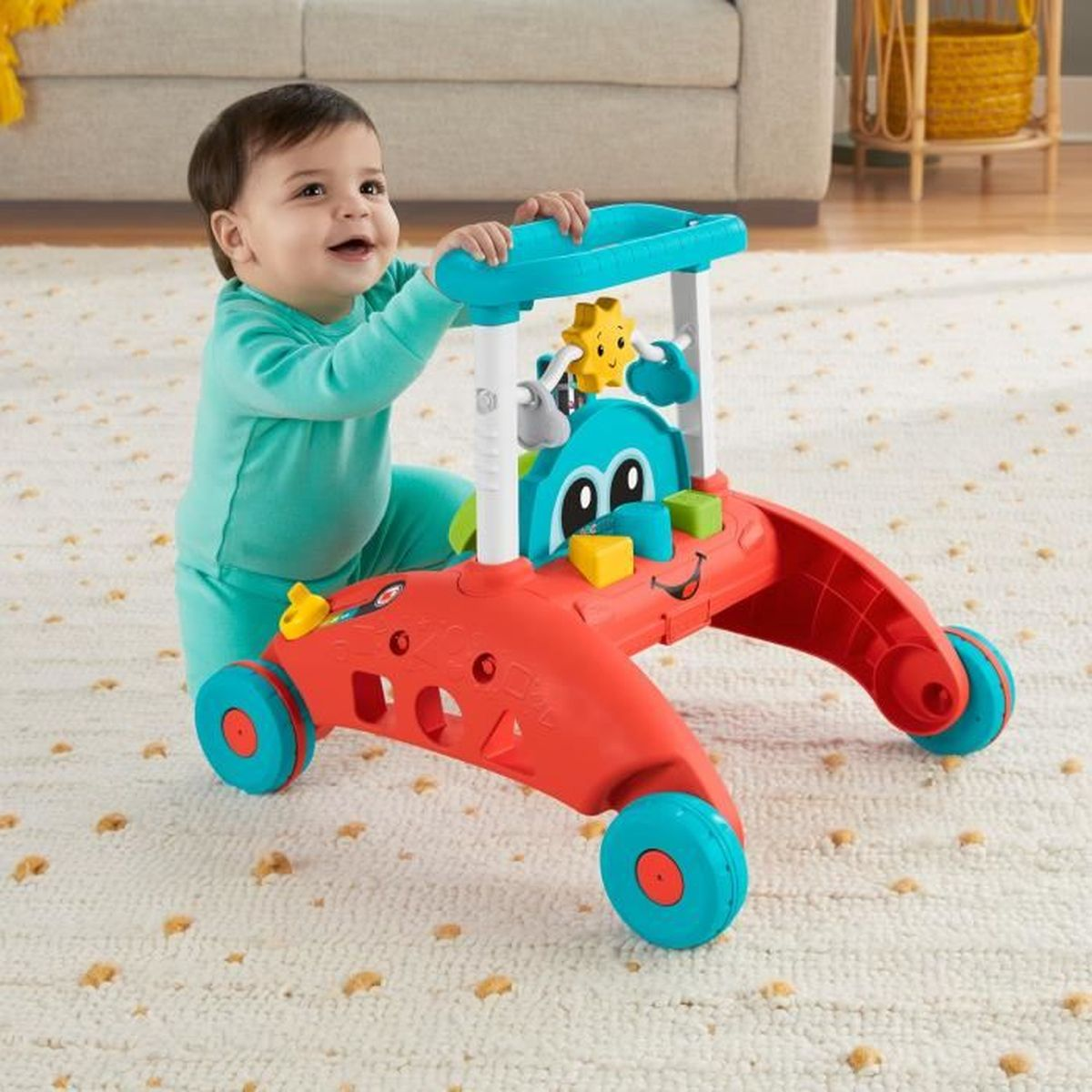 Ein Baby in türkiser Kleidung hält einen bunten rot-blauen Lauflernwagen auf einem Teppichboden.