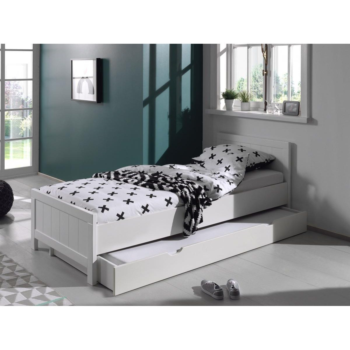 Ein weißes Bett mit schwarz-weißem Kreuzemuster und einer Schublade darunter in einem hellen, modernem Zimmer.