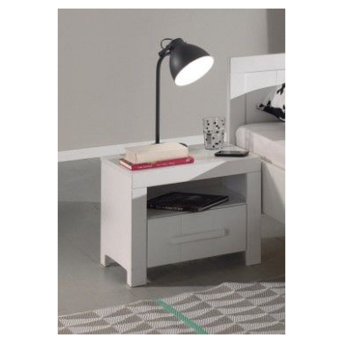 Ein weißer Nachttisch mit einer schwarzen Schreibtischlampe, Büchern und einem Glas davor.