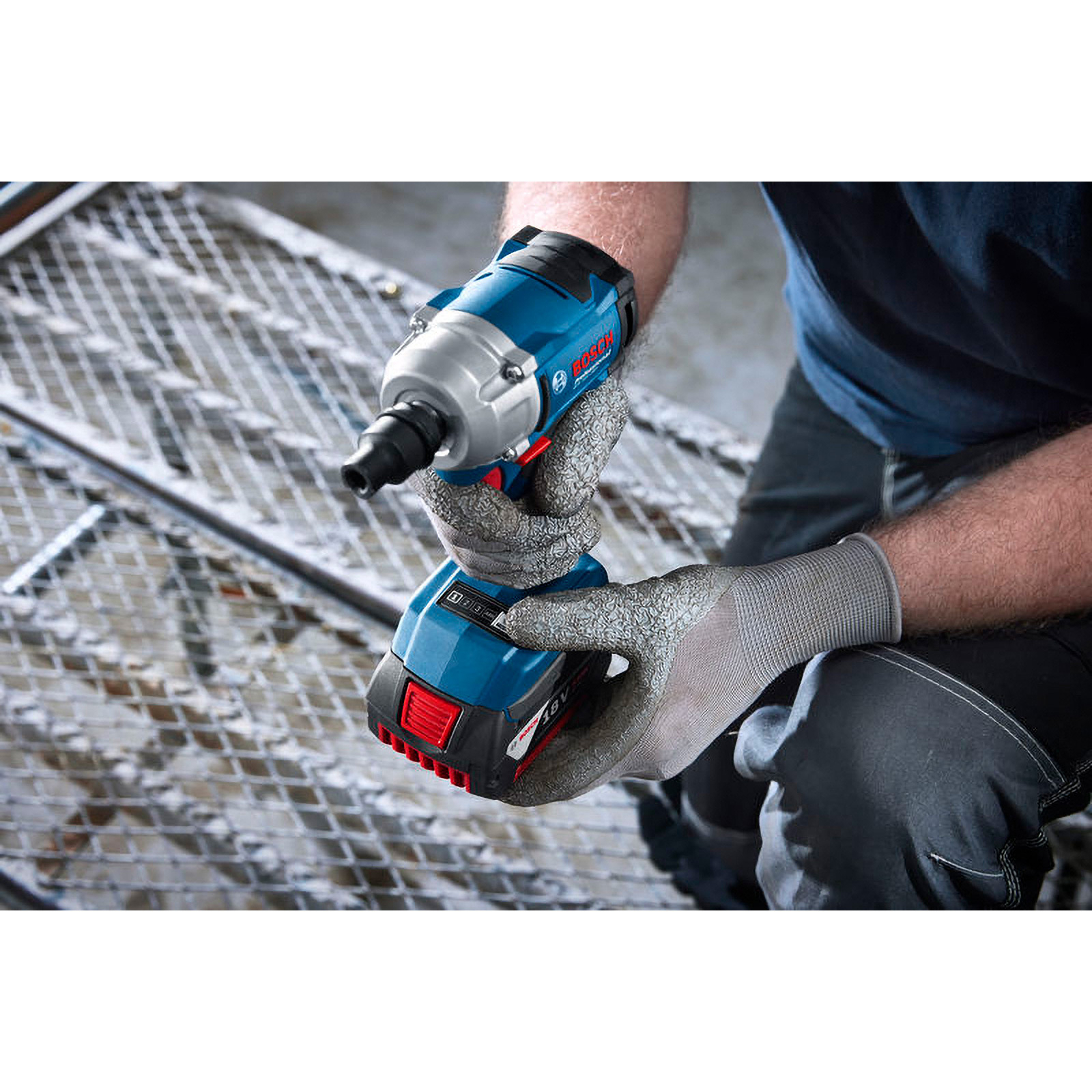 Eine Person mit Arbeitshandschuhen hält einen blau-silbernen Akku-Schlagschrauber über ein Metallgitter.