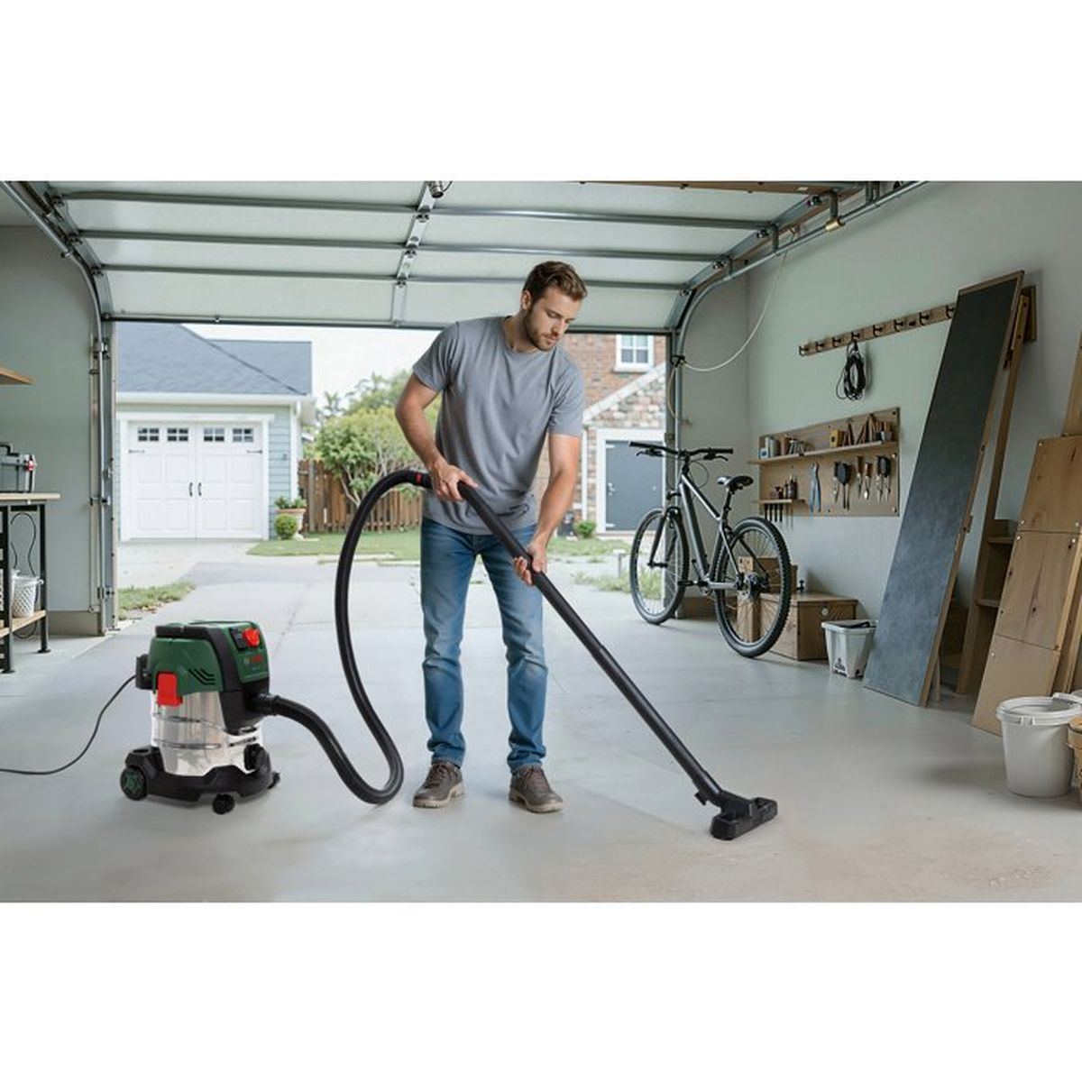 Ein Mann in grauen Shirt und Jeans saugt mit einem Nass-Trockensauger den Boden seiner Garage.