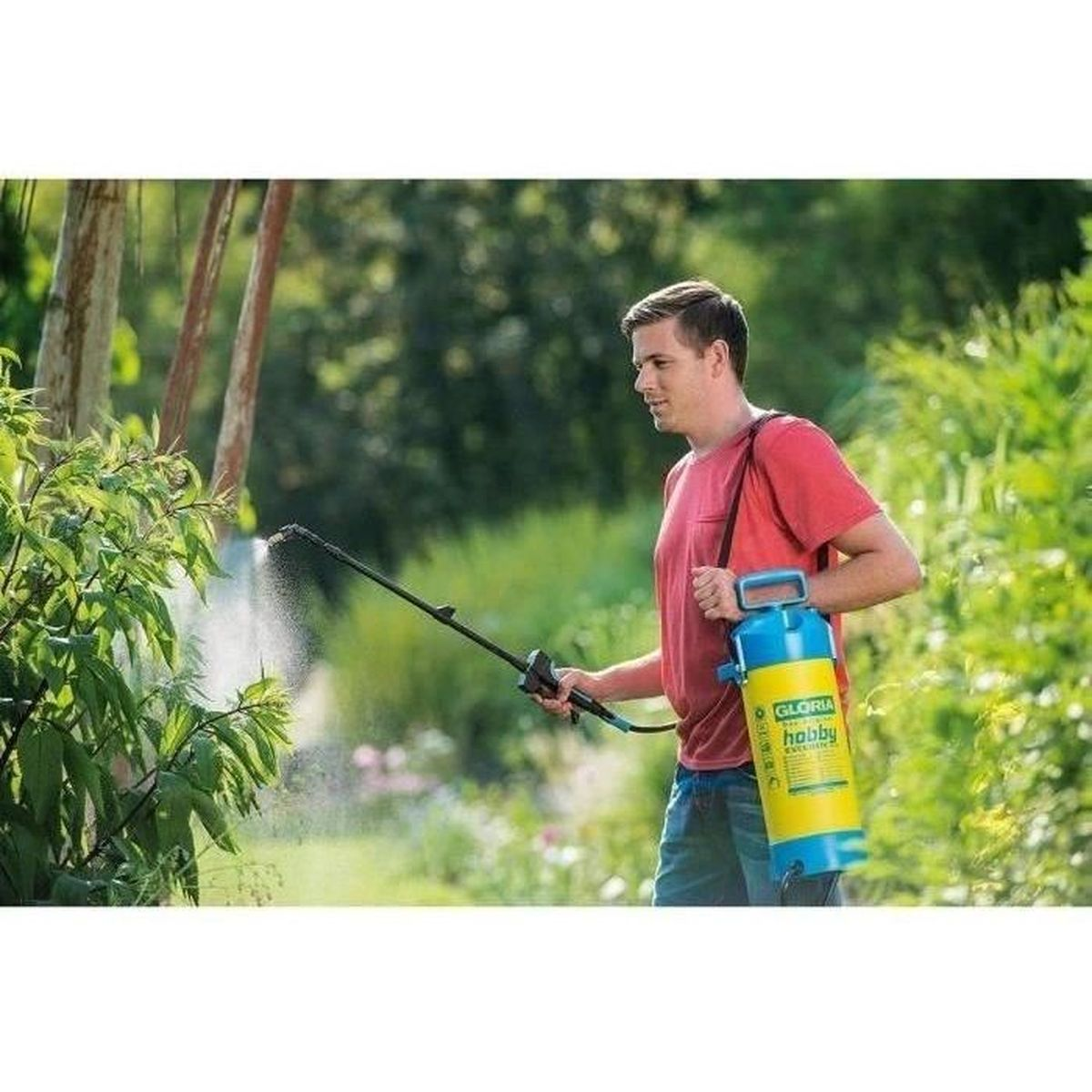 Ein Mann im roten Shirt besprüht Pflanzen in einem üppigen Garten mit einem gelb-blauen Drucksprüher.