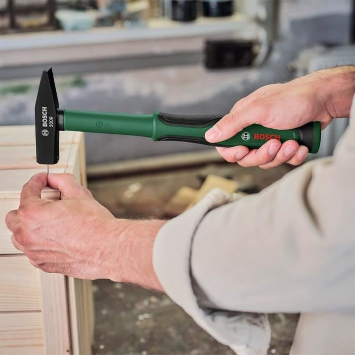 Ein Mensch hält einen grünen Bosch-Hammer in der Hand und schlägt einen Nagel in ein Holzmöbel.