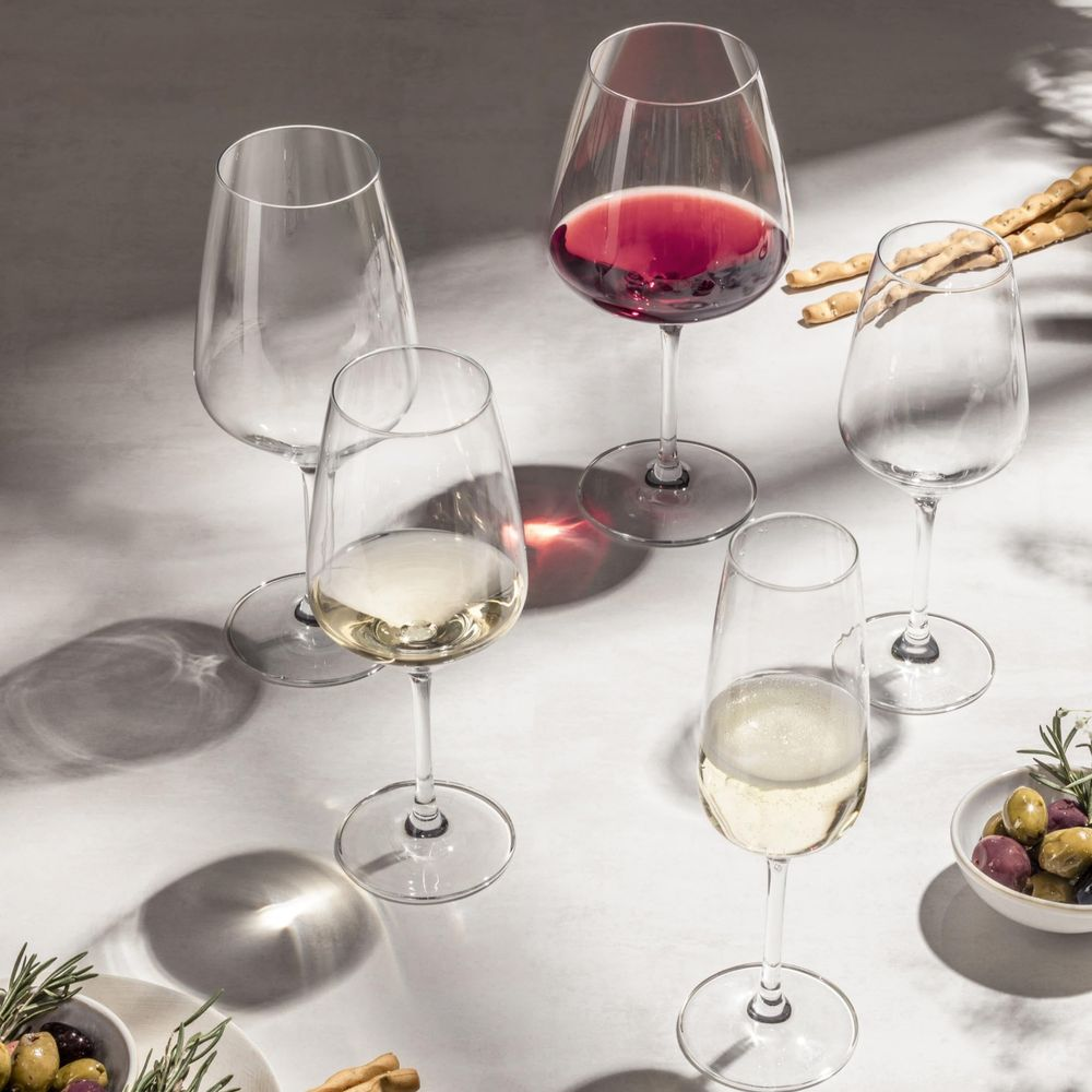Fünf Wein- und Champagnergläser auf heller Oberfläche mit Brotstangen und Schüsseln mit Oliven.