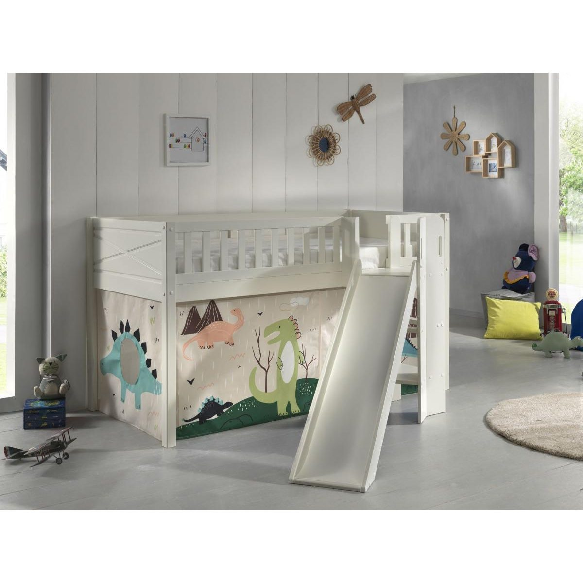 Ein weißes Hochbett mit Rutsche und bunten Dinosaurier-Vorhängen in einem hellen Kinderzimmer.