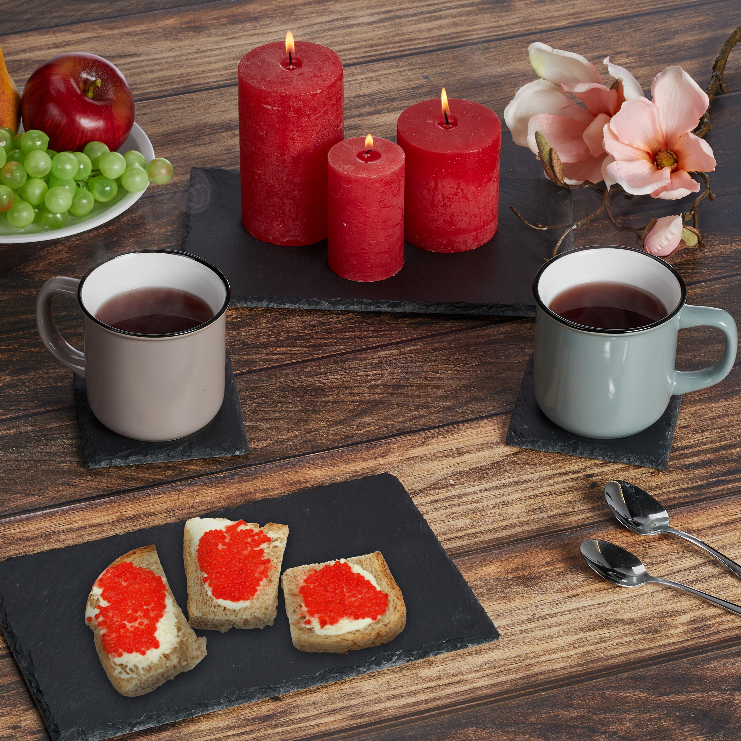 Tassen Tee, rote Kerzen, Brote mit rotem Kaviar und Obst auf einem Holz Tisch.