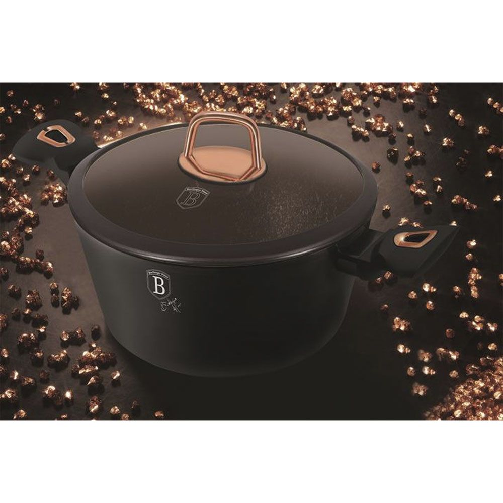 Une casserole noire avec des poignées et un bouton de couvercle couleur cuivre sur fond sombre.