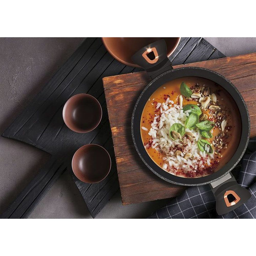 Une poêle avec de la soupe, du riz, des herbes et des noix sur une planche en bois.