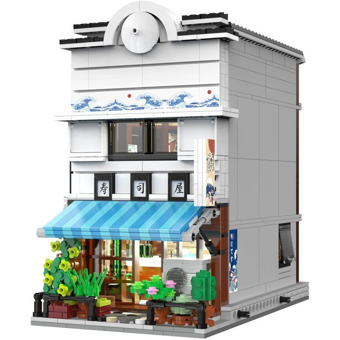 Ein detailreiches Lego-Gebäude mit weißer Fassade, blauem Sonnenschutz und grünen Pflanzen im Eingangsbereich.