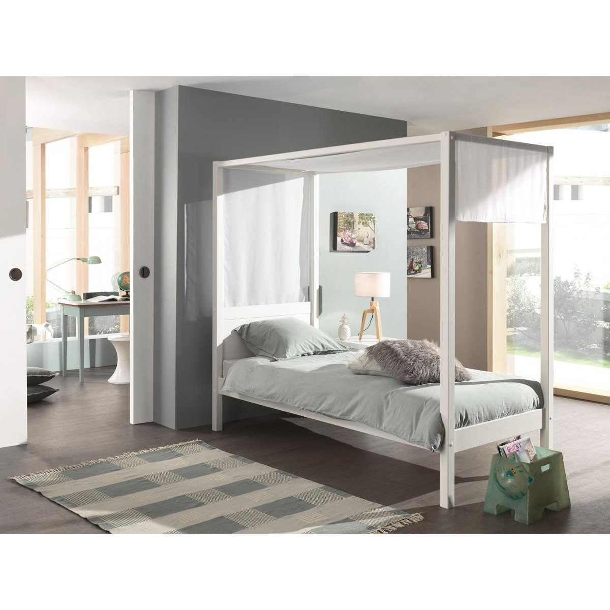 Ein weißes Himmelbett mit grauer Bettwäsche in einem modern eingerichteten Zimmer mit großem Fenster und Teppich.