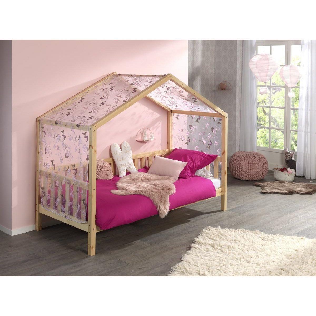 Ein Kinderbett mit Hausrahmen, rosa Bettwäsche und Vorhang in einem hellen Zimmer.