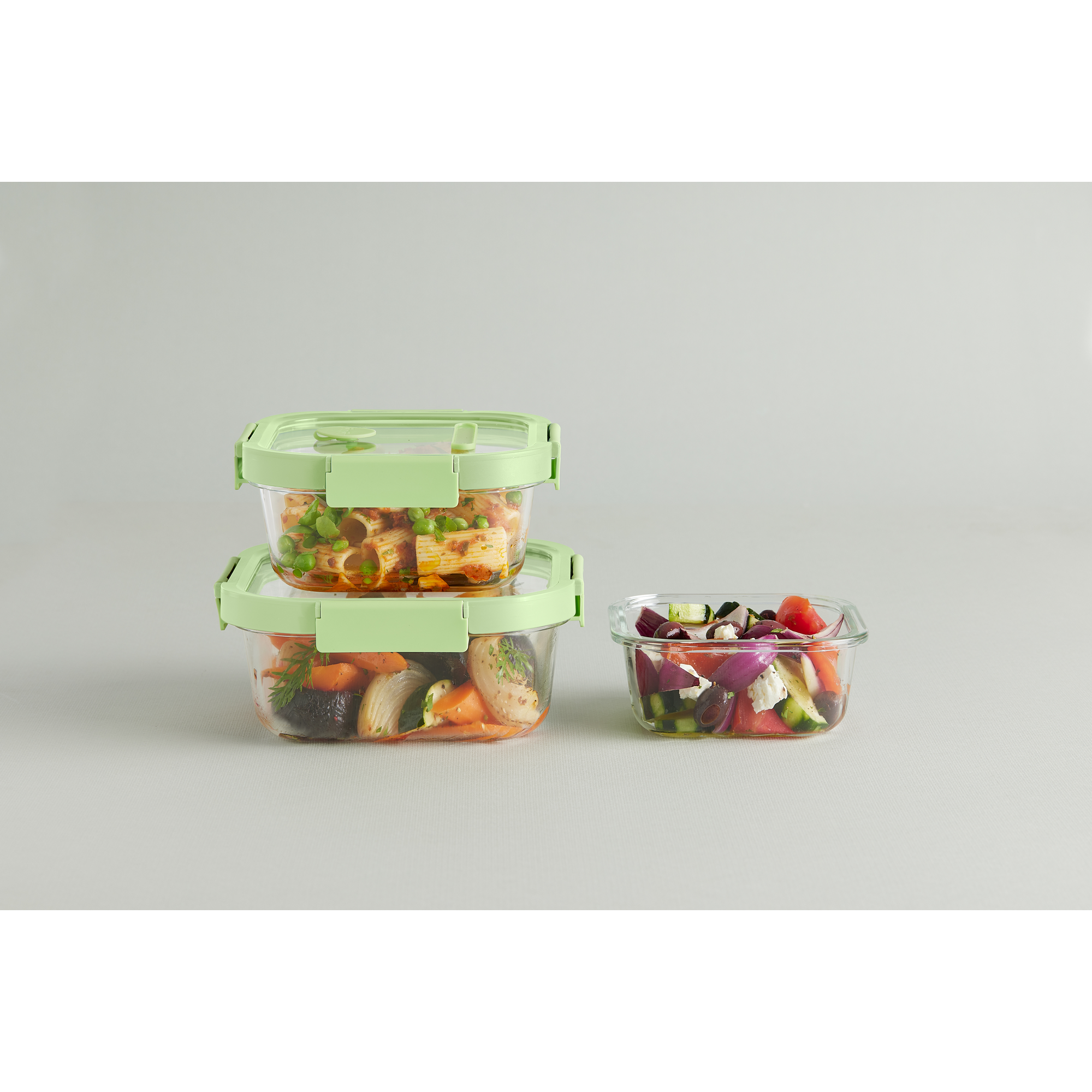 Drei Glasbehälter mit grünem Deckel gefüllt mit Nudeln und Salat auf neutralem Hintergrund.