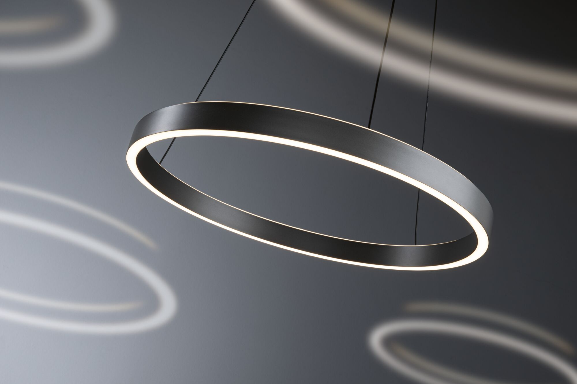 Eine moderne schwarze ringförmige Pendelleuchte hängt vor dunklem Hintergrund mit verschwommenen Lichtreflexen.