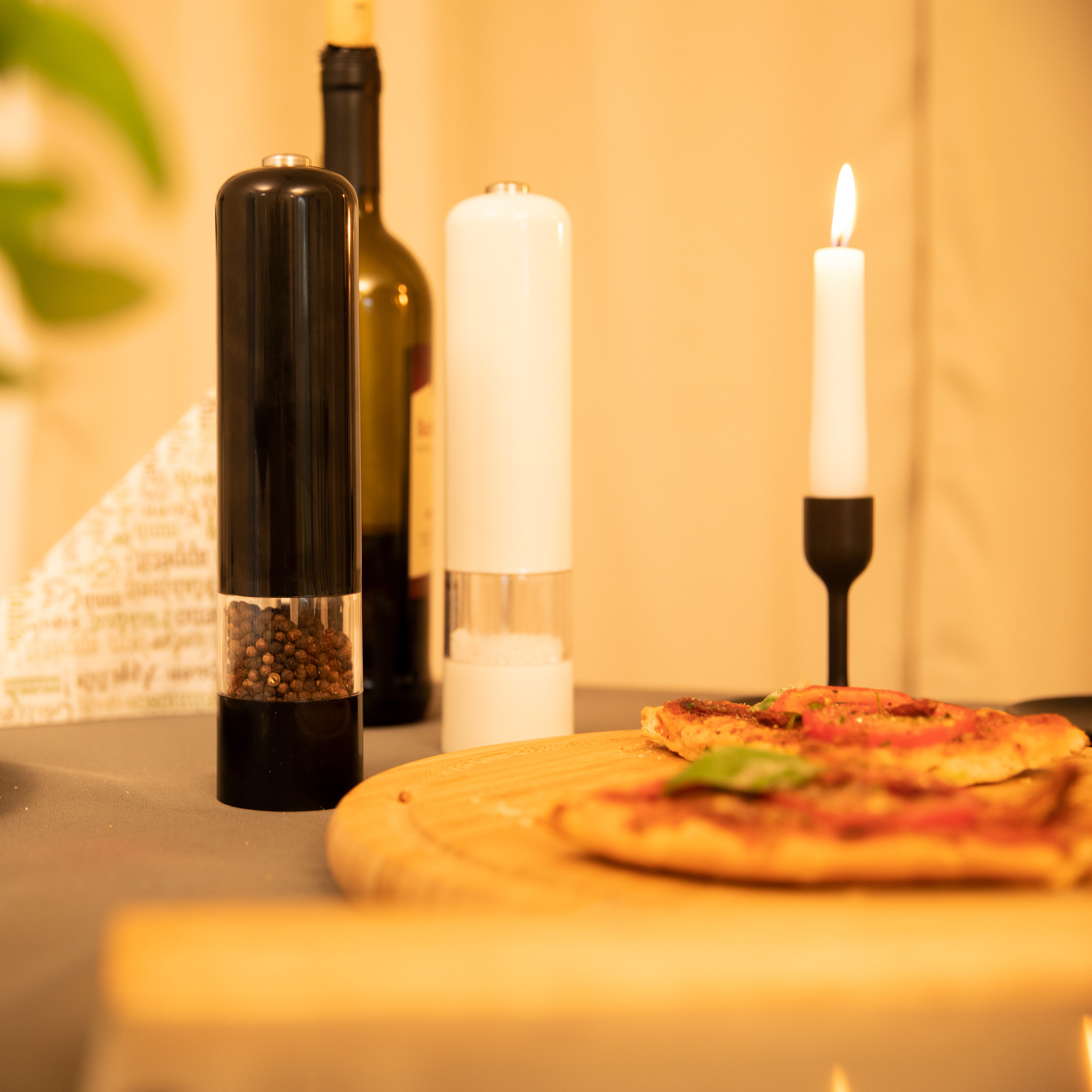 Ein Holzbrett mit Pizza, Salz- und Pfeffermühlen, einer Weinflasche und einer brennenden Kerze.