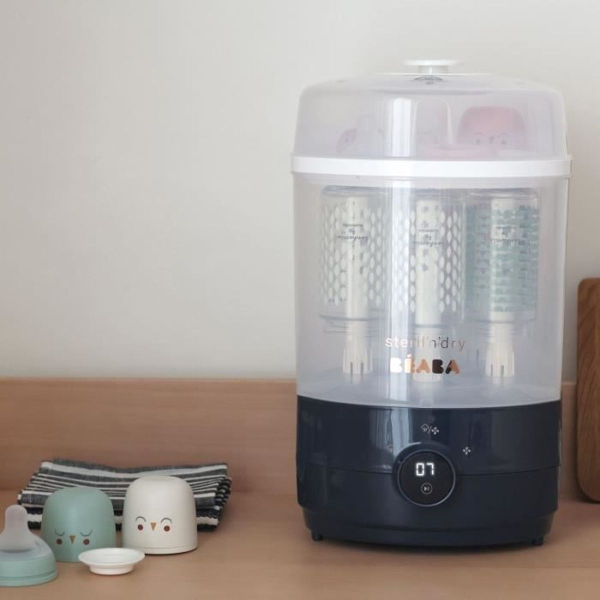 Ein weiß-dunkelblauer Sterilisator für Babyflaschen mit digitaler Anzeige steht auf einer Holztheke.