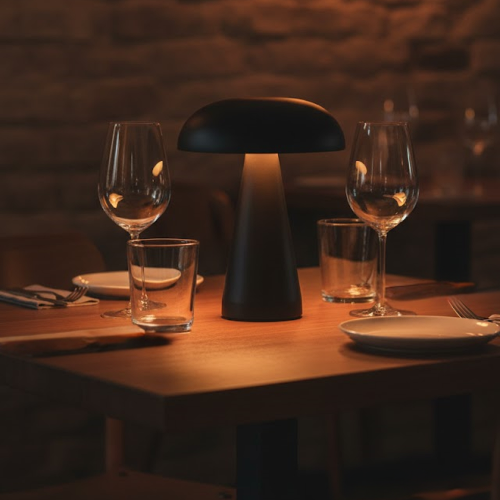 A black mushroom-shaped lamp on a wooden restaurant table, surrounded by glasses, plates, and cutlery.