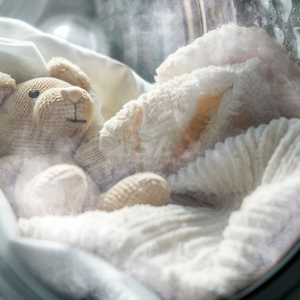 Un pequeño osito de peluche y ropa blanca dentro del tambor humeante de una lavadora.