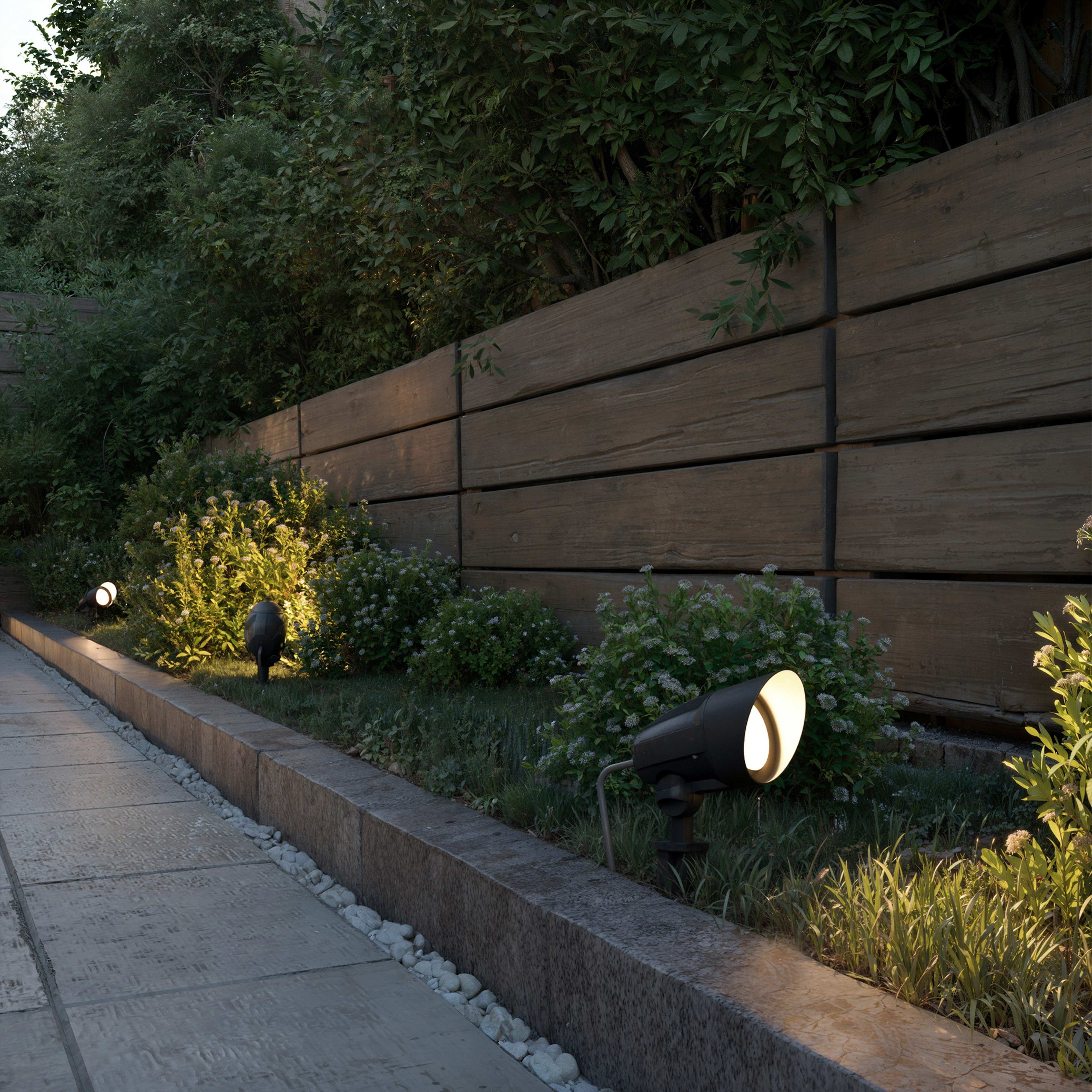 Een verlicht pad met spots langs een houten schutting en struiken.